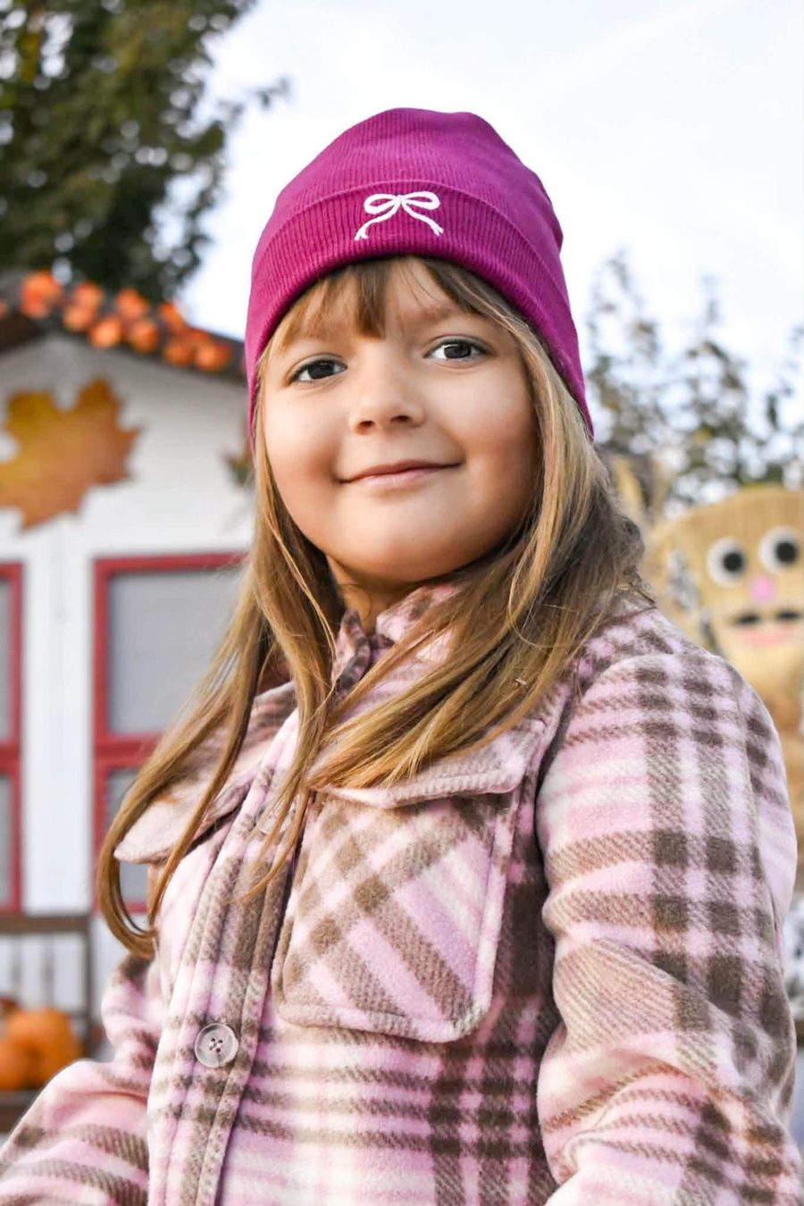 Mosolygó kislány bordó sapkában, mögötte őszi díszítés